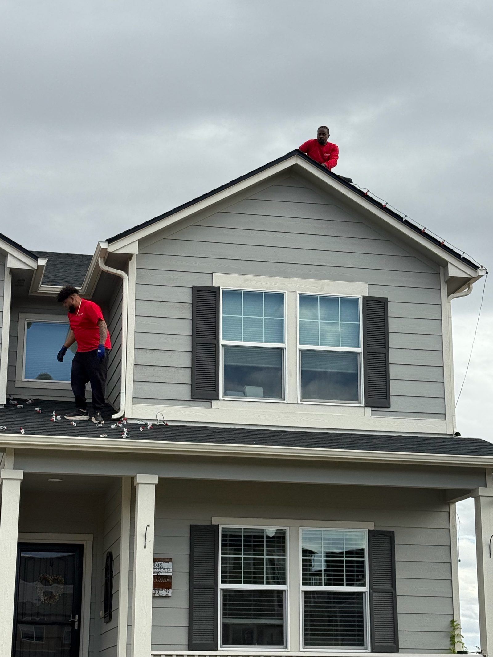 Our installers on roof peak hanging holiday lights on a gray two-story house Our installers on roof peak hanging holiday lights on a gray two-story house