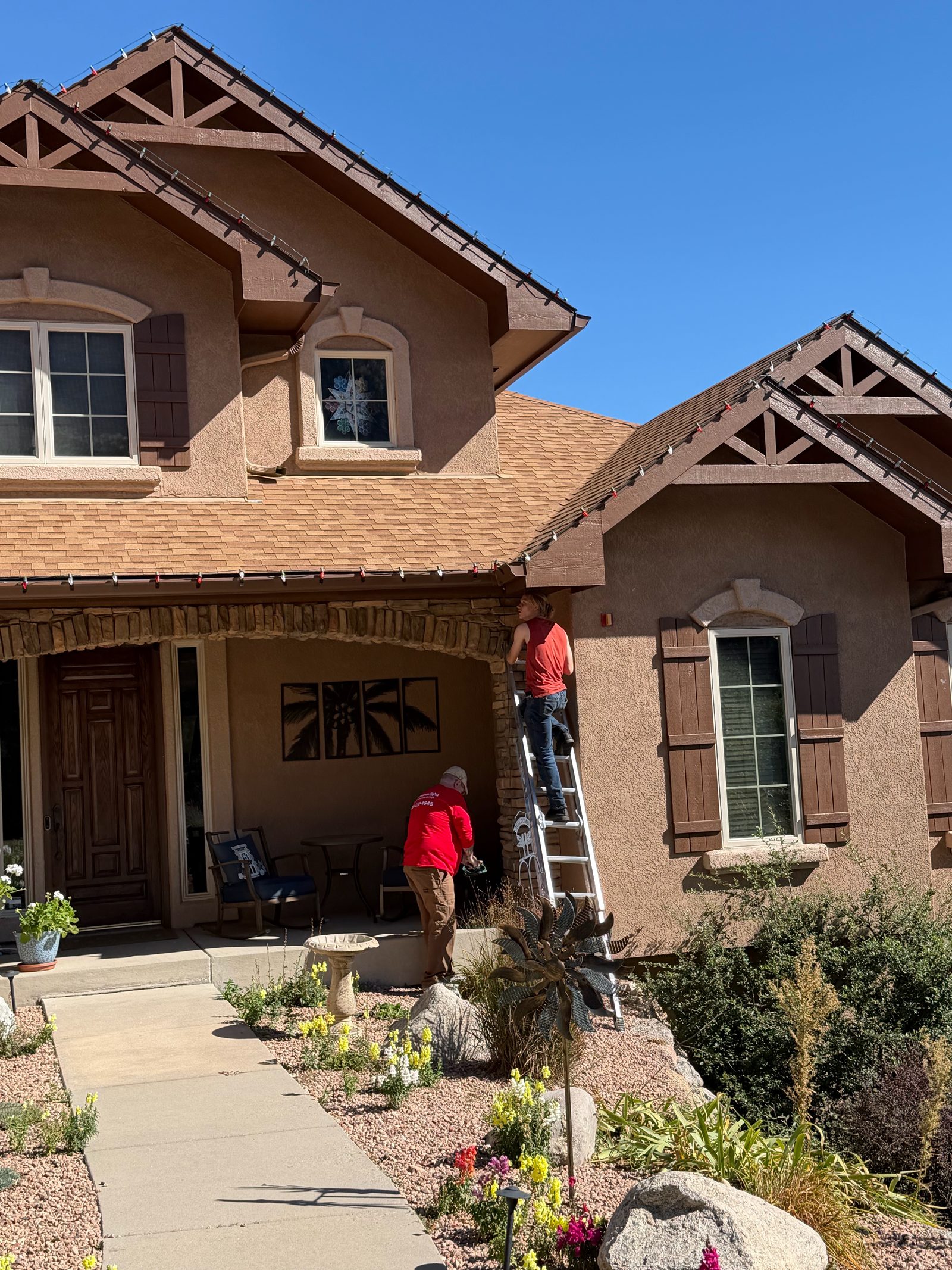 Christmas light installers on ladder hanging red Christmas lights on a residential home Christmas light installers on ladder hanging red Christmas lights on a residential home